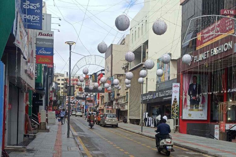 Welcome 2023: Bengaluru's New Year Shine Is Back This Year... 88 Commercial Street in the morning. Mostly vacant except for a few passersby. A scooter in the foreground. Chinese lanterns hung over the street.
